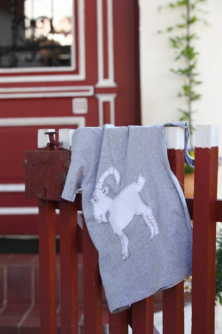 Graues Shirt mit selbstgenähtem Tiermotiv auf Holzzaun hängend