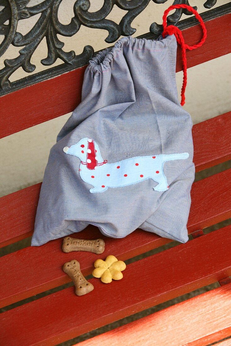 Cloth bag with hand-sewn, appliqué sausage dog motif and dog biscuits on garden bench