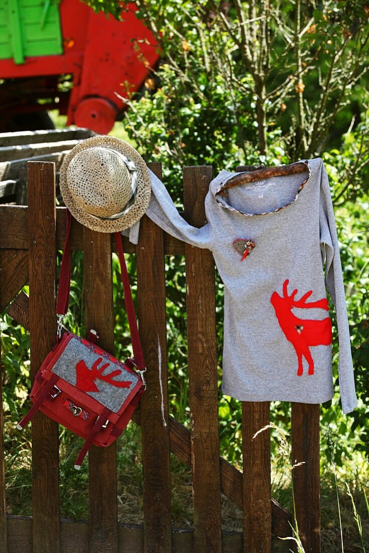 T-shirt & handbag with appliqué red stag motifs hanging on wooden fence
