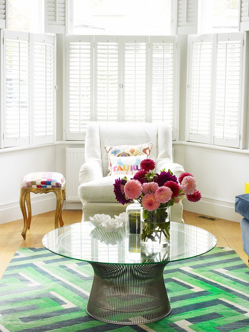 60s table on rug with geometric pattern and armchair in bay window with interior shutters