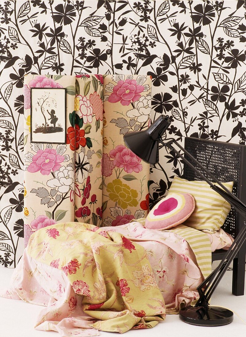 Romantic bed linen on chaise longue and floral screen against black and white wallpaper combined with simple retro lamp