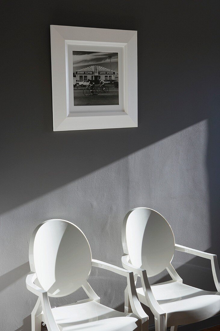 Two white designer chairs against grey wall