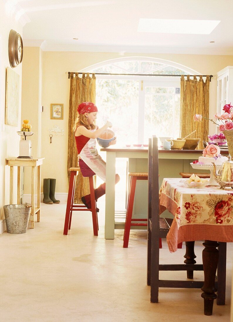 Junges Mädchen bei Küchenarbeit auf Barhocker sitzend in einer Landhausküche