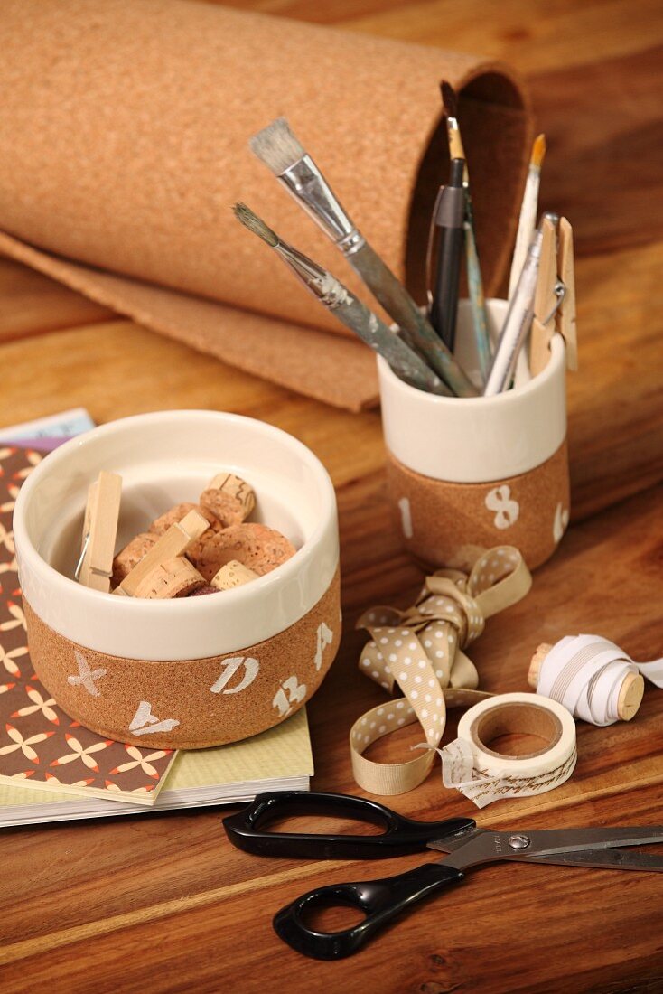 Bastelutensilien neben verschiedenen Behältern mit Korkstücken und Pinseln auf Holztisch