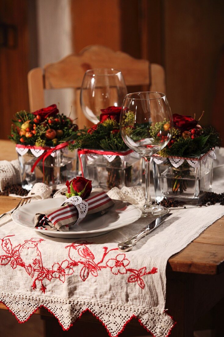 Gedeck mit Stoffserviette und Weinglas vor Weihnachtsgesteck auf besticktem Tischläufer