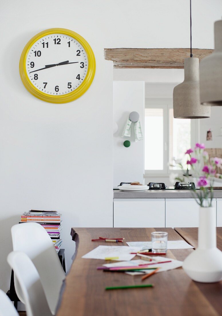 Drawing utensils on dining table with yellow-framed station clock next to hatch leading to kitchen