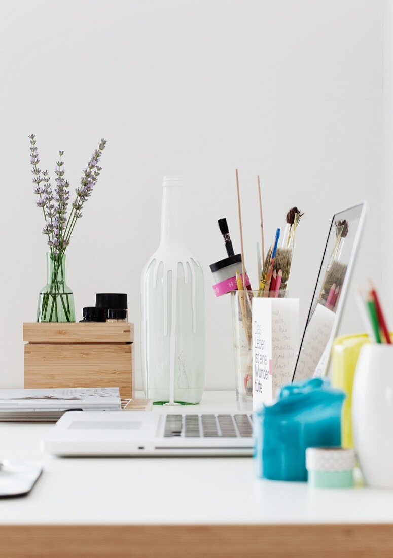 Kleiner Arbeitsplatz mit Laptop, Schreibutensilien und Vasen auf Tisch