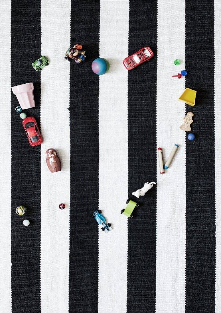Spielsachen herzförmig auf schwarzweiss gestreiftem Teppich aufgestellt