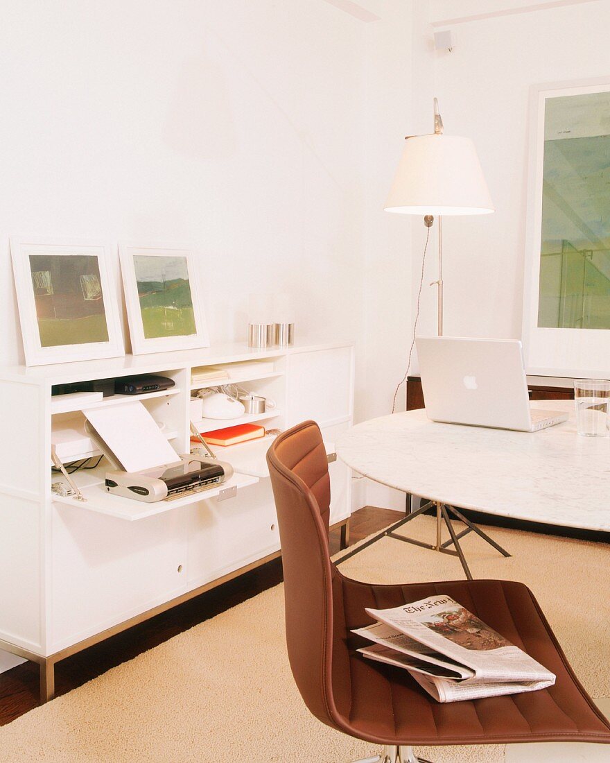 Weisses Arbeitszimmer mit Stauraum in Sideboard; Drehstuhl und Laptop auf rundem Tisch