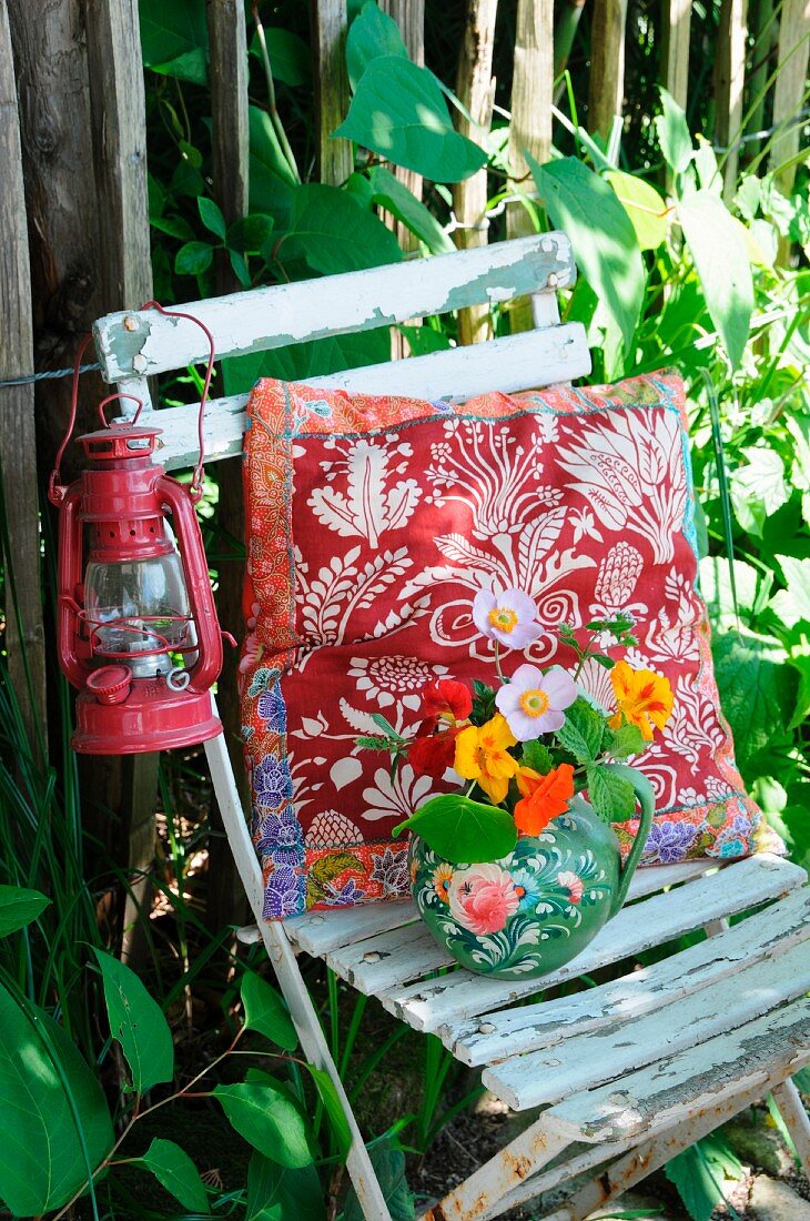 Cushion, lantern & posy in jug on old garden chair