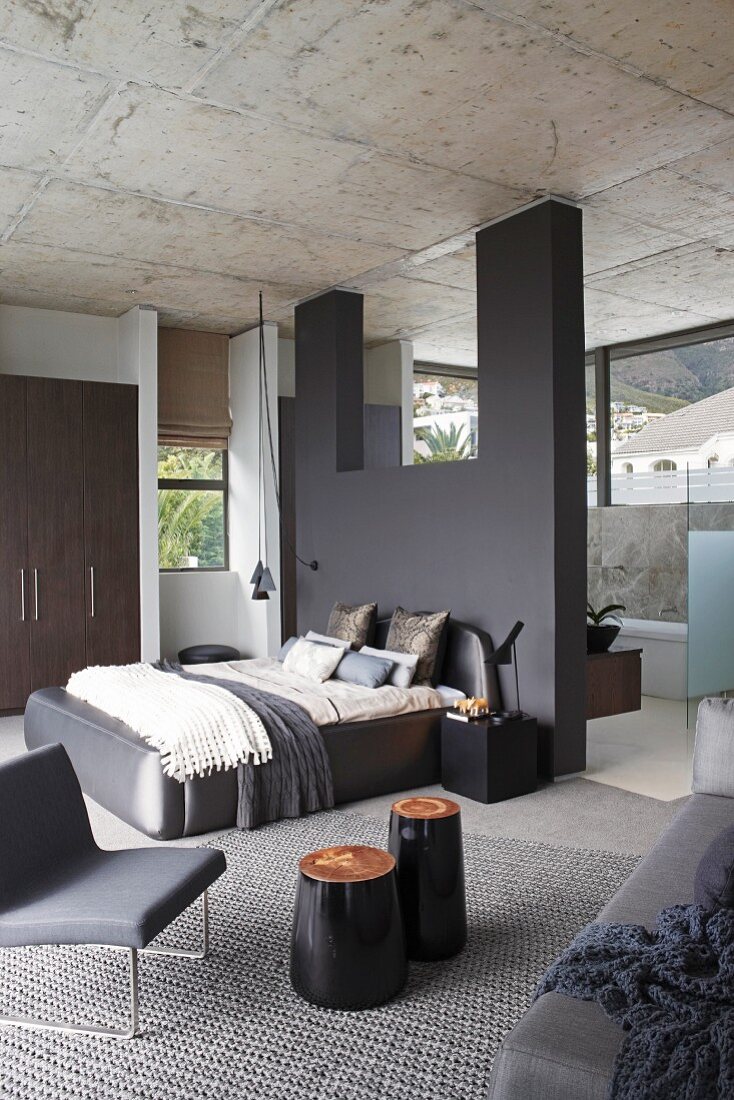 Elegantes puristisches Designer-Schlafzimmer mit dunkelgrauer Wandscheibe, Durchblick zur Bad-Ensuite mit Fensterband und durchgehender Betondecke