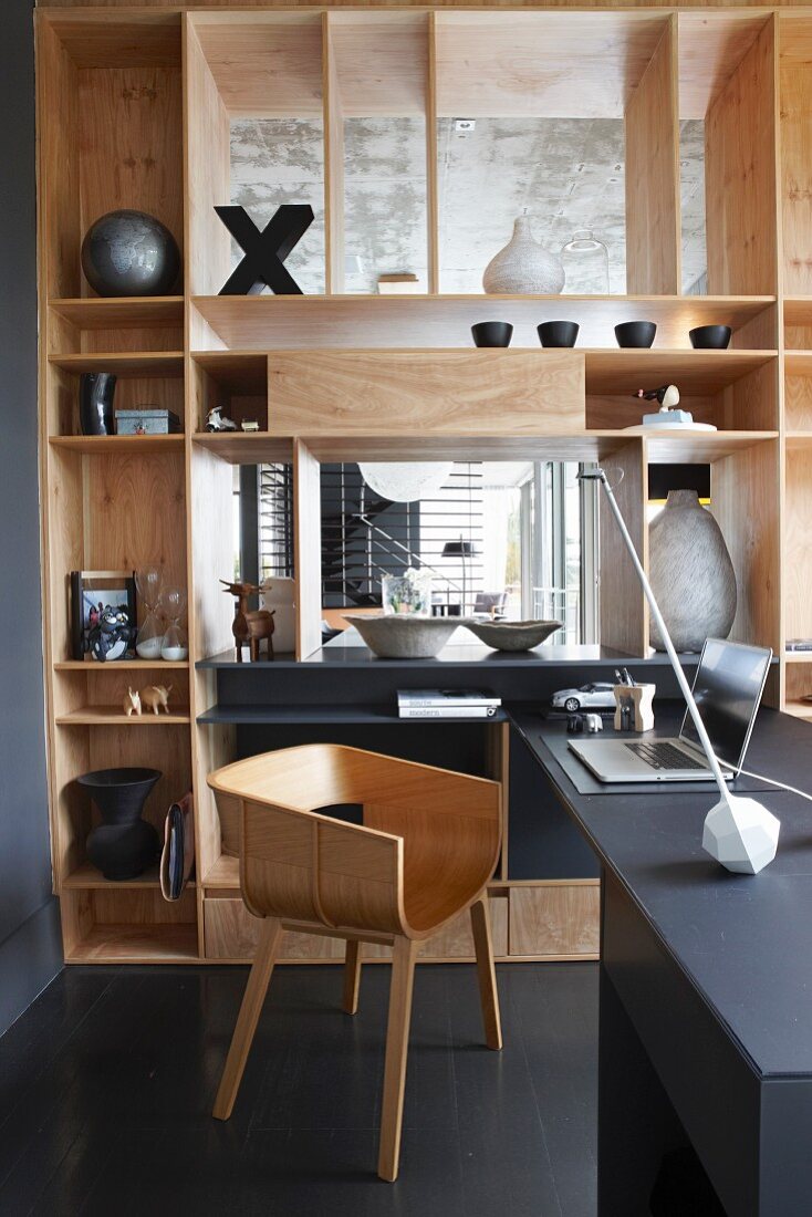 Stilvoller Homeofficeplatz mit Designer-Holzschalenstuhl und elegantem eingebautem Raumteilerregal