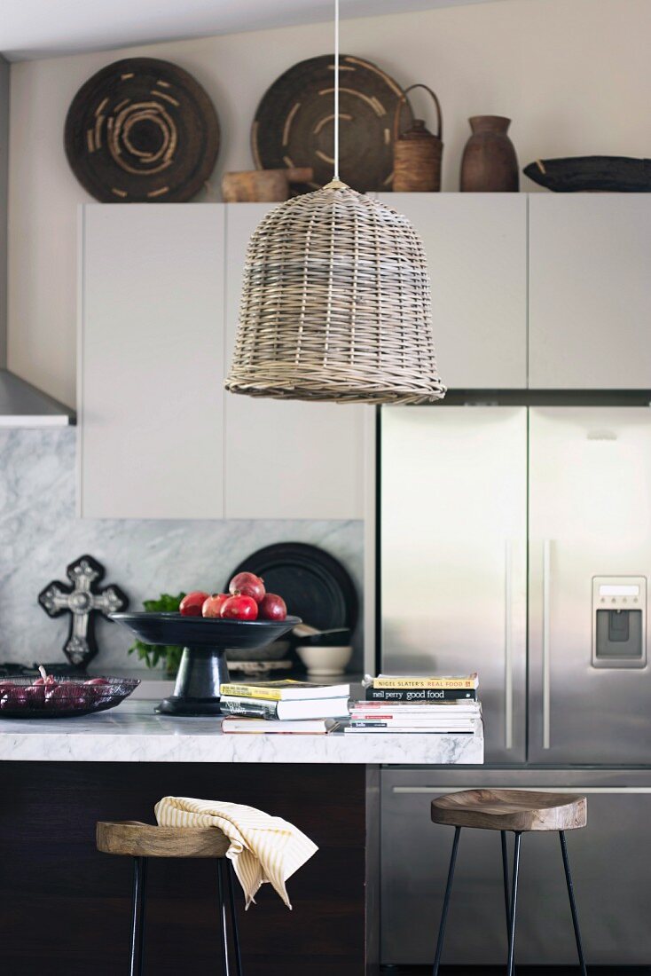 Korblampe über Küchentheke mit Marmorplatte, Bücherstapel neben Obstschale; im Hintergrund afrikanische Körbe auf weissen Hängeschränken