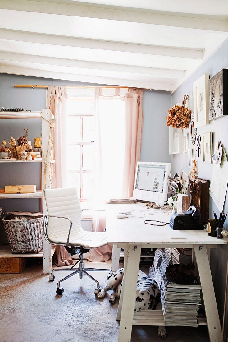 Weiß lackierter Holztisch mit PC und Büroutensilien, davor moderner Drehstuhl mit weißem Lederbezug, in hellgrau getöntem Zimmer mit weisser Holzbalkendecke