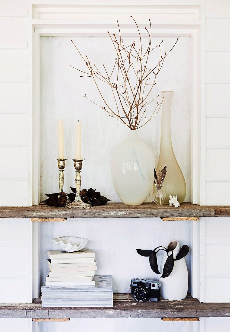 Rustikale Holzbords, darauf Vasen, Kerzenständer und Bücherstapel, eingebaut in Wandnische einer weisslackierten Holzwand