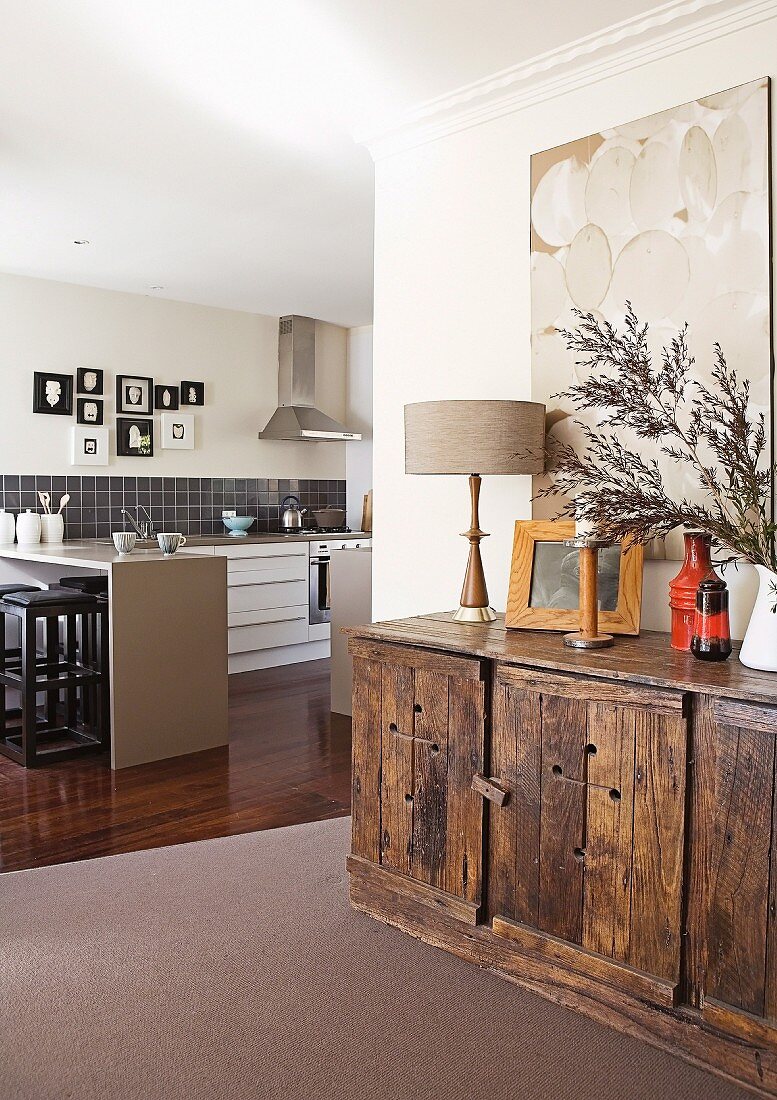 Artwork above ornaments on rustic sideboard in front of free-standing counter in open-plan kitchen