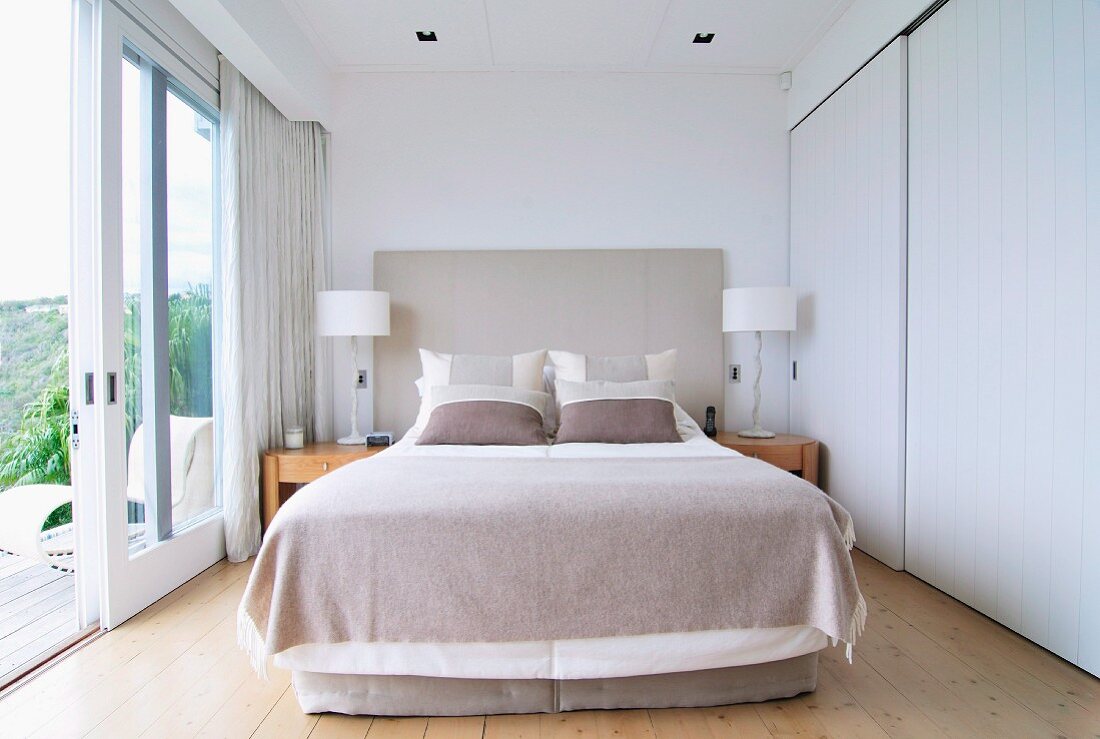 Double bed, fitted wardrobes with white sliding doors and open terrace doors in bright bedroom with view of landscape