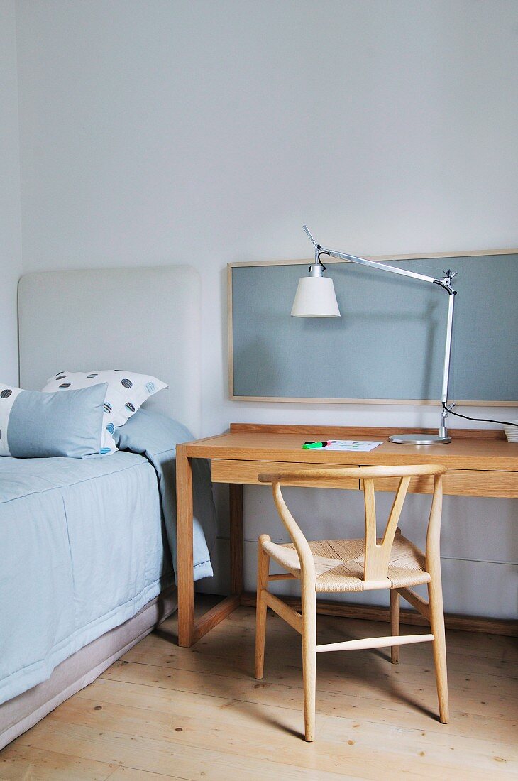 Reduzierter Home-Office Platz mit Designerleuchte, Holzstuhl und Schreibtisch neben Einzelbett in schlichtem, stilvollem Ambiente