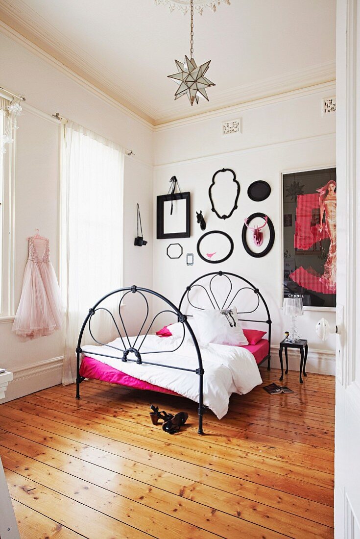 Black wrought iron bed on rustic wooden floor in white bedroom
