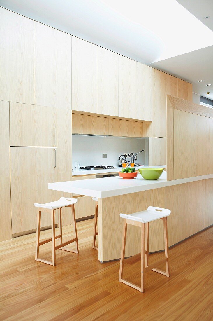 Kitchen area - fitted cupboards with seamless wooden fronts, counter with screen of same wood and bar stools with white shell seats and wooden frames