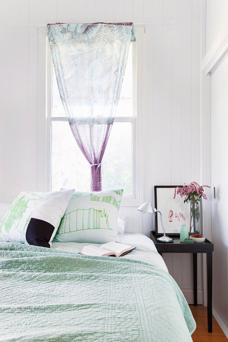 Schlafzimmer in blassen Farben, Bett vor dem Fenster mit Tuch