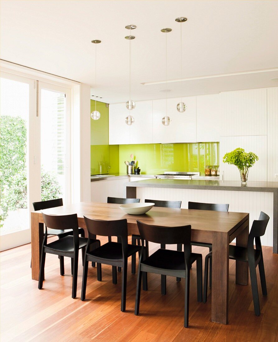 Massiver Holzesstisch vor weißer Designerküche mit hellgrünem Spritzschutz und Terrassenzugang