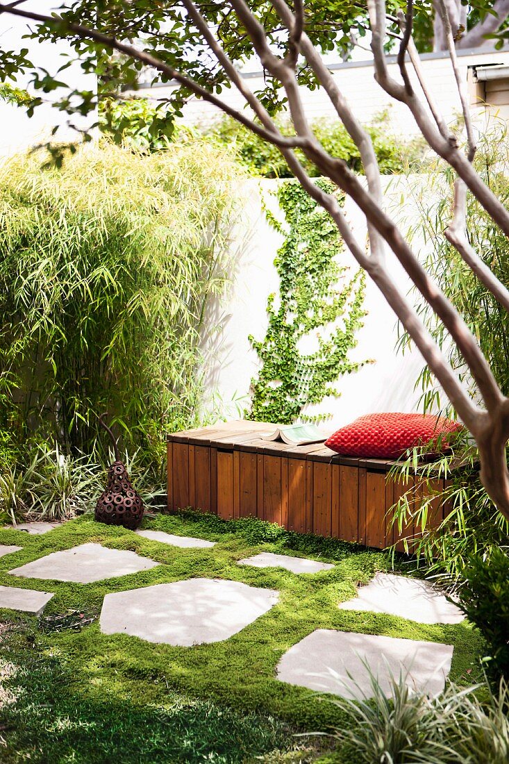 Gemütlicher Rückzugsort im sommerlichen Garten mit Holzsitzbank und rotem Polsterkissen