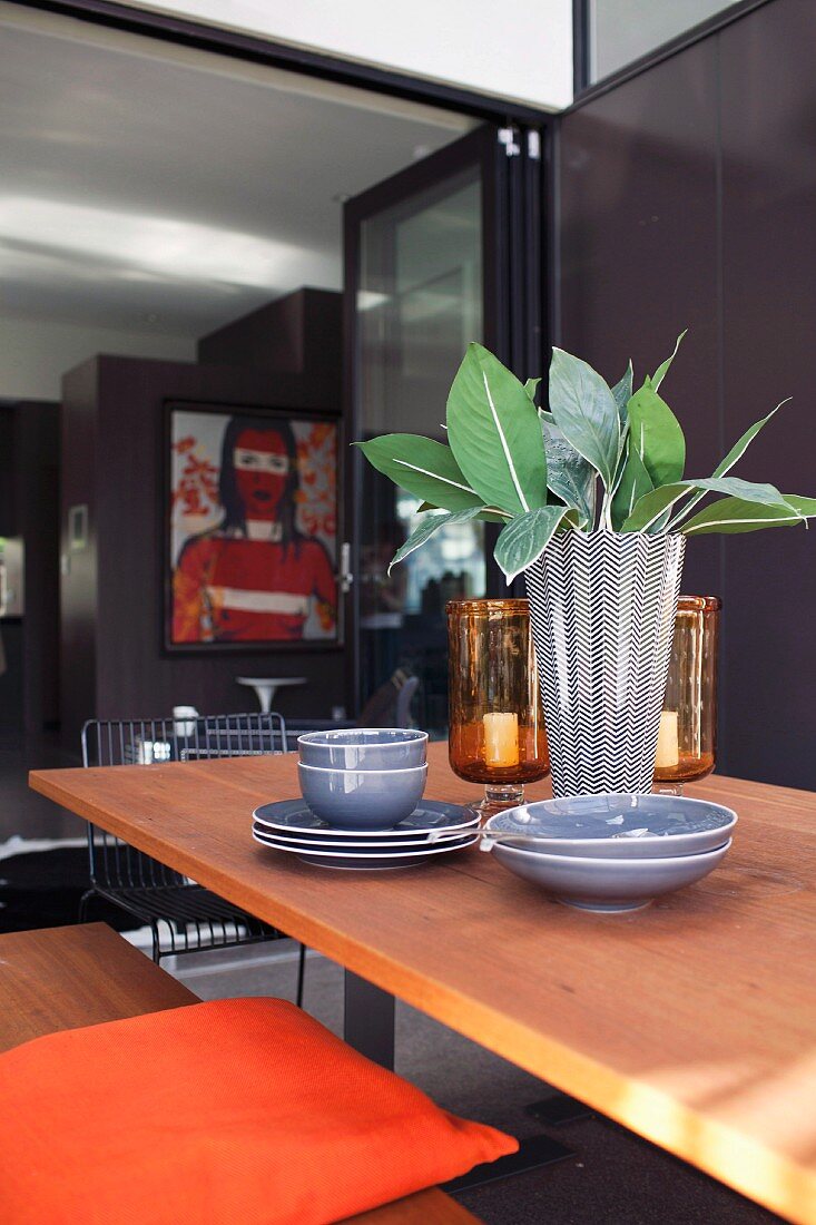 Esstisch mit grauem Geschirr und schwarz-weißer Designer-Vase mit Blättern dekoriert vor geöffneter Schiebefalttür