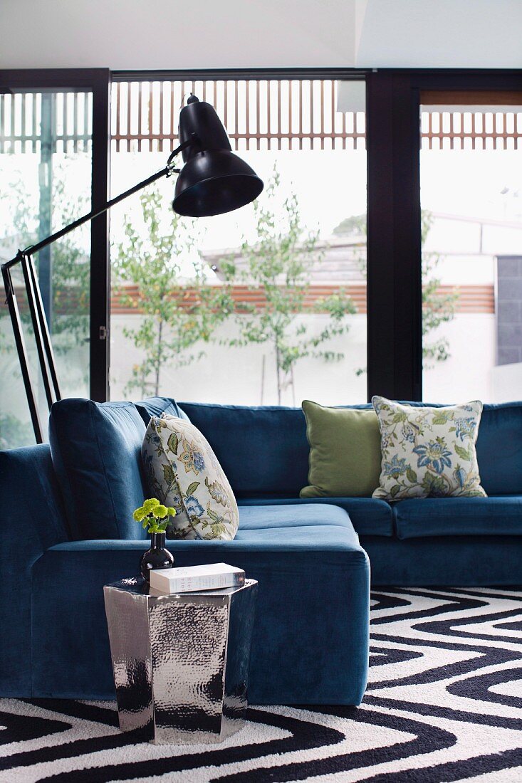 Comfortable grey-blue corner sofa, retro standard lamps and shiny side table in front of glass walls