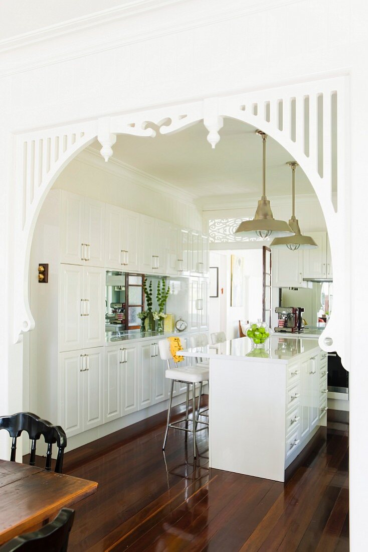 Blick vom Essplatz in die weiße Landhausküche mit weiß lackiertem verziertem Durchgang