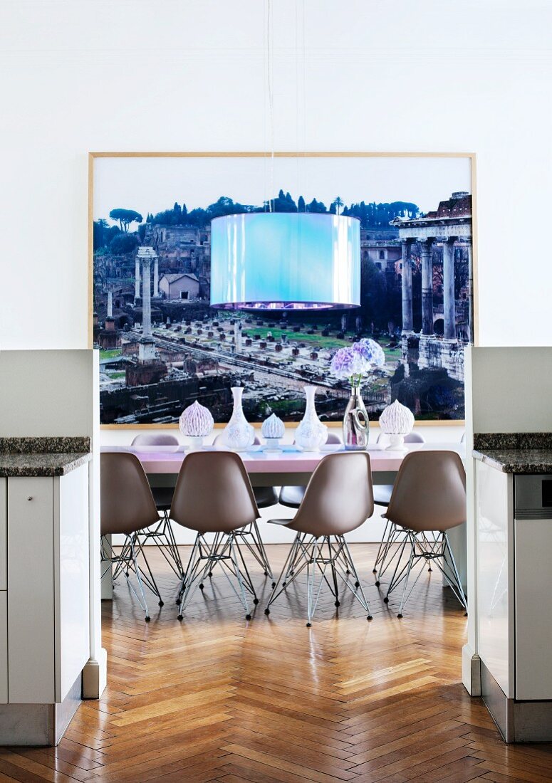 Blick zwischen halbhohen Küchenelementen auf Essplatz mit Eames-Stühlen und Designerleuchte vor grossformatigem Foto des Forum Romanums