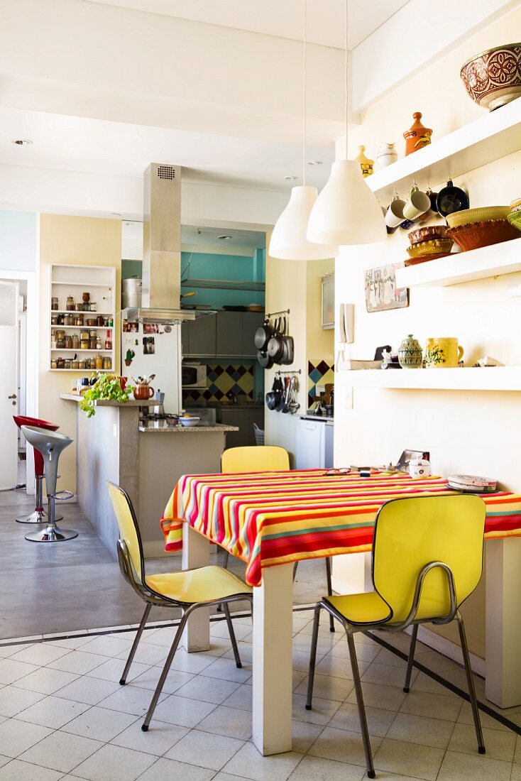 Kleiner Essplatz mit gelben Vintage Stühlen in grosser Wohnküche mit Frühstücksbar im Hintergrund