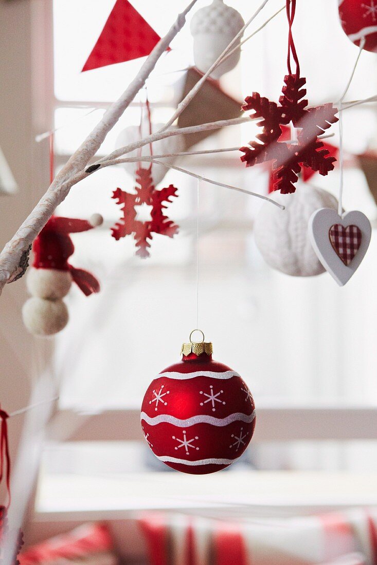Red and white Christmas decorations hanging from branches with window in blurred background