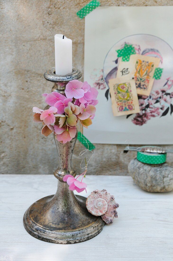 Hydrangea florets threaded on silver wire and seashell decorating patinated candlestick; nostalgic collage in background