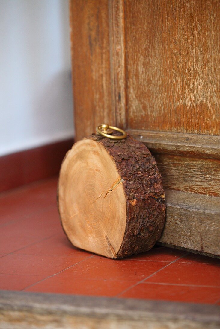 Unten abgeflachte Baumscheibe mit eingeschraubtem Messingring als rustikaler Türstopper