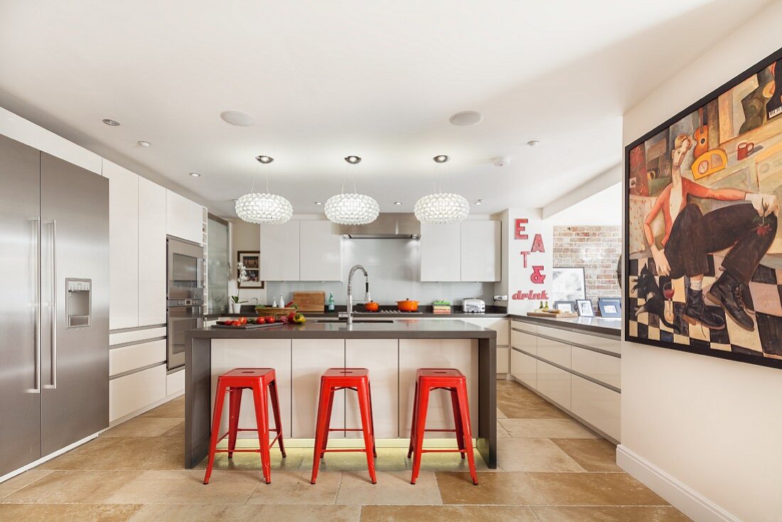 Designer kitchen with island counter, red bar stools, modern painting on wall and wall aperture leading to dining area