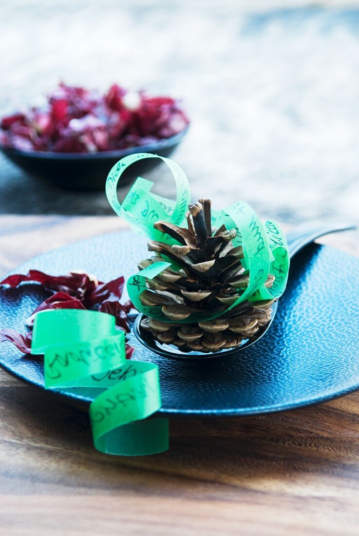 Fir cones and green ribbon used as menu on blue plate
