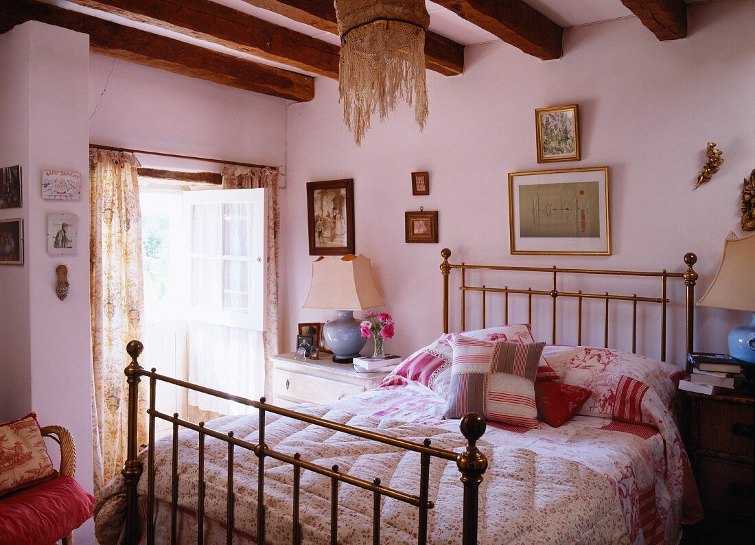 Handgenähte Decken und Kissen auf Messingbett im romantischen Schlafzimmer eines historischen Bauernhauses