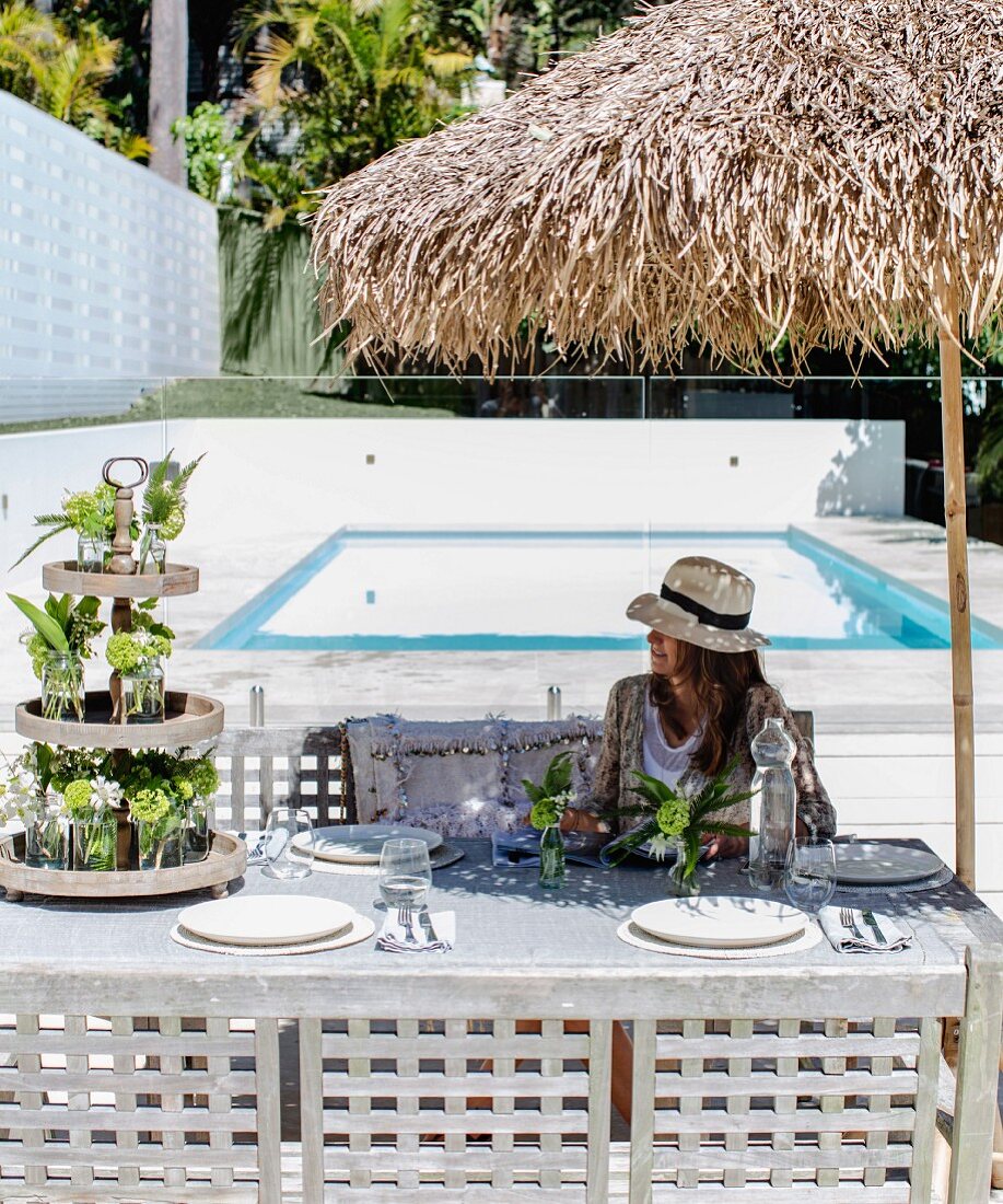 Woman sitting at festively set table below parasol next to pool