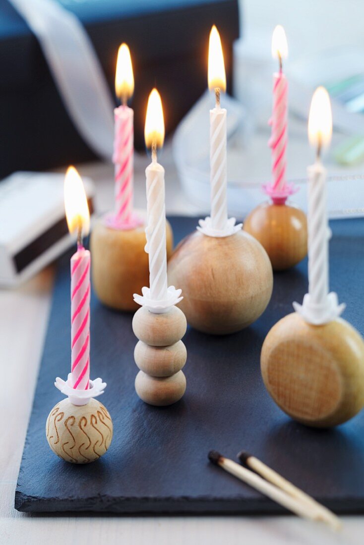 Kerzenständer aus Holzkugeln mit brennenden Kerzen auf Schieferplatte