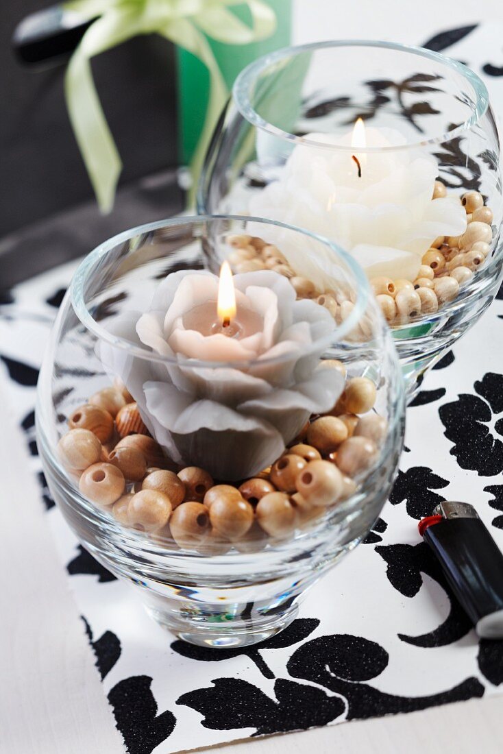 Candle lanterns with flower-shaped candles on wooden beads on black and white place mat