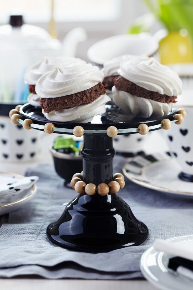 Filled meringues on black glass cake stand decorated with strings of wooden beads