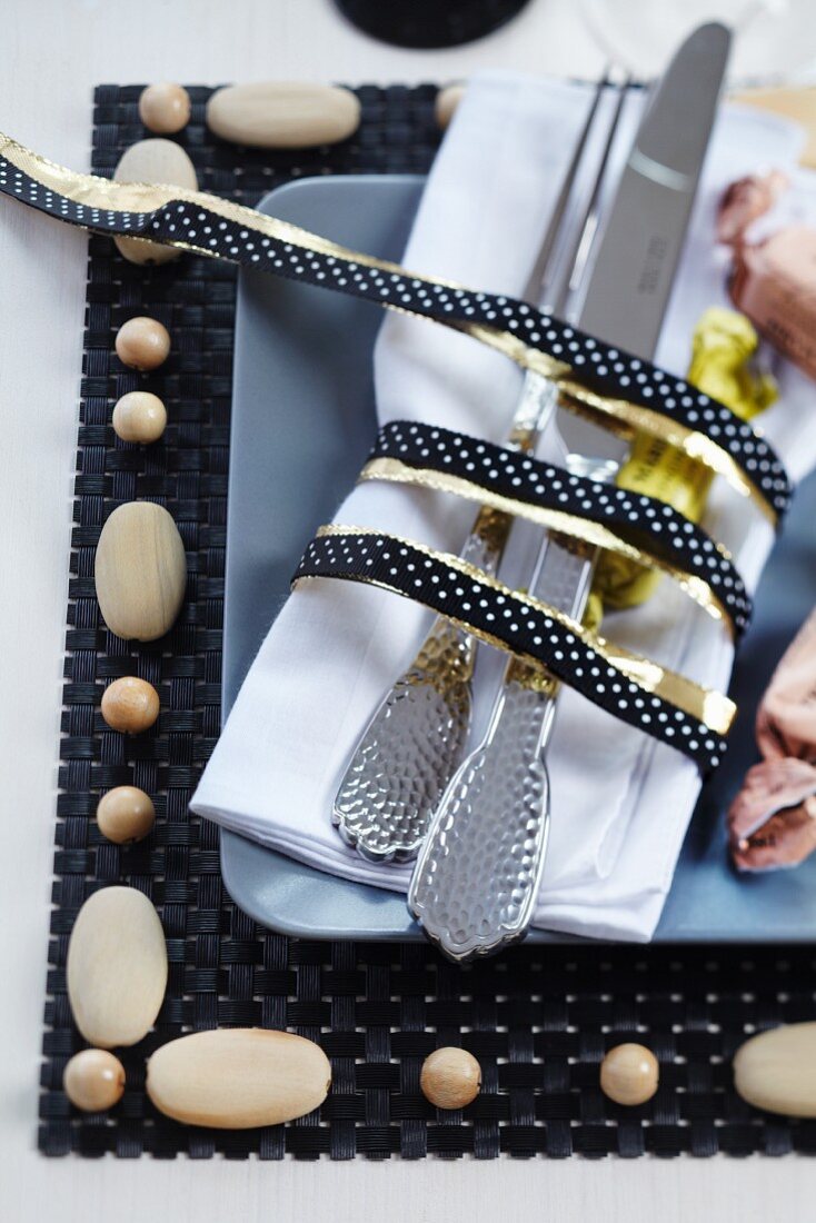 Cutlery and napkin tied with black and gold ribbon on place mat with wooden beads