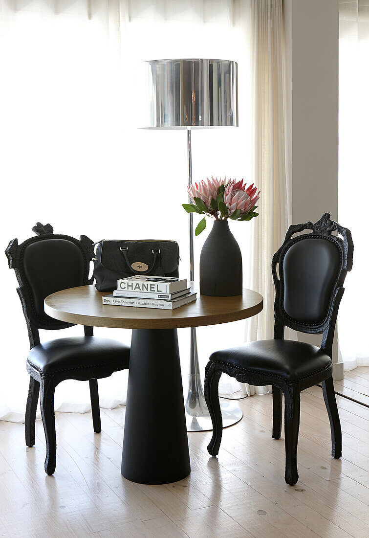 Two black designer chairs around a round table, silver-colored floor lamp in the background