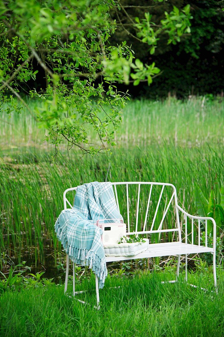 Filigrane Gartenbank aus weißem Metall mit Decke und Polster auf einer Wiese in ländlicher Umgebung