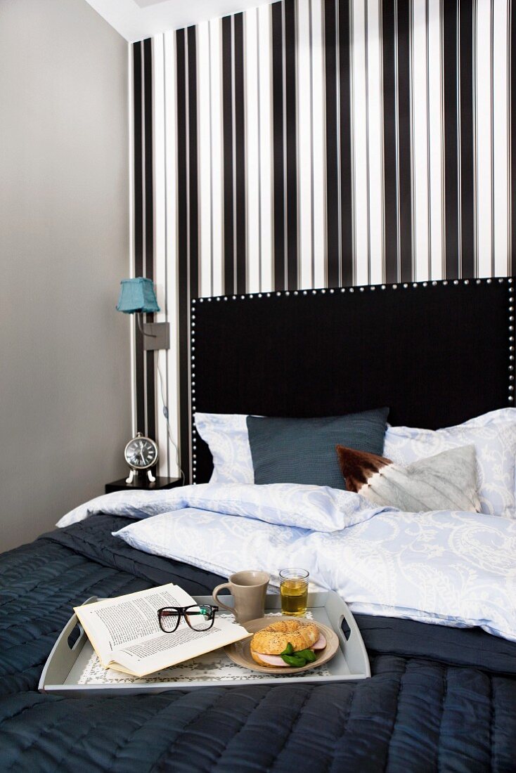Frühstückstablett auf schwarzer Tagesdecke im Bett, mit schwarzem Kopfteil, elegante, schwarzweisse Streifentapete an Wand