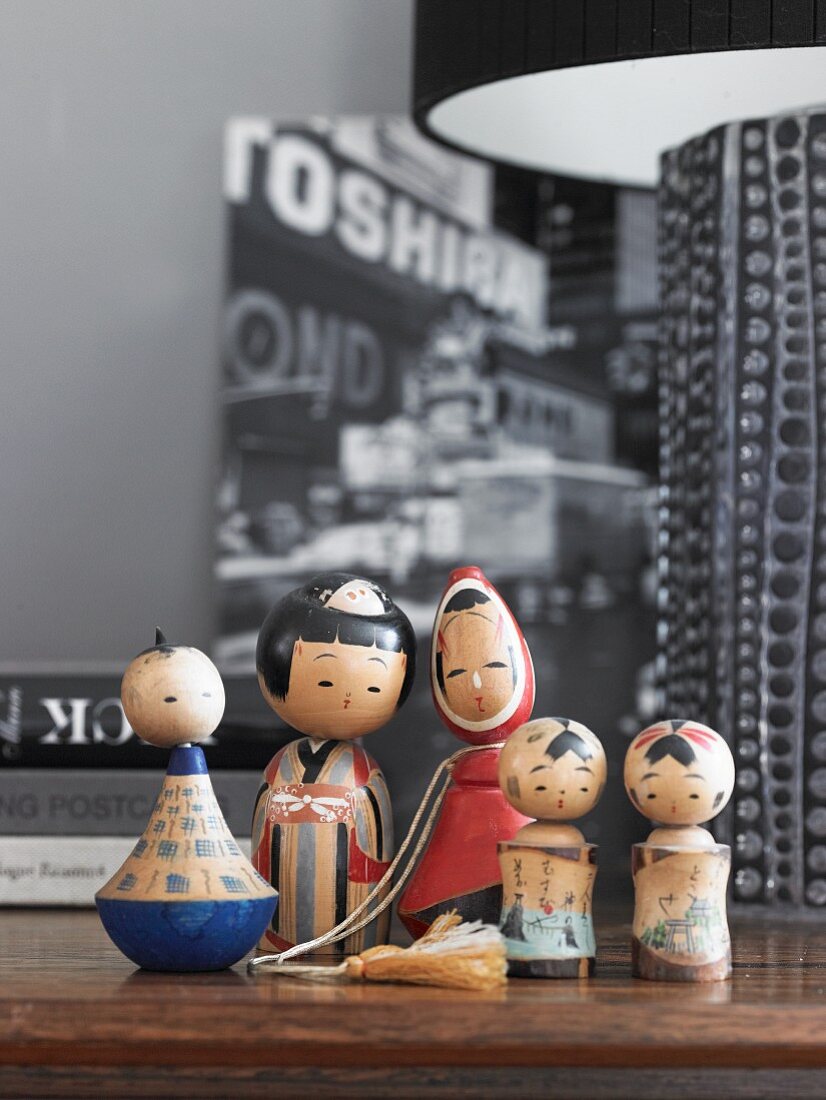 Family of wooden, painted Kokeshi dolls on wooden surface next to partially visible table lamp
