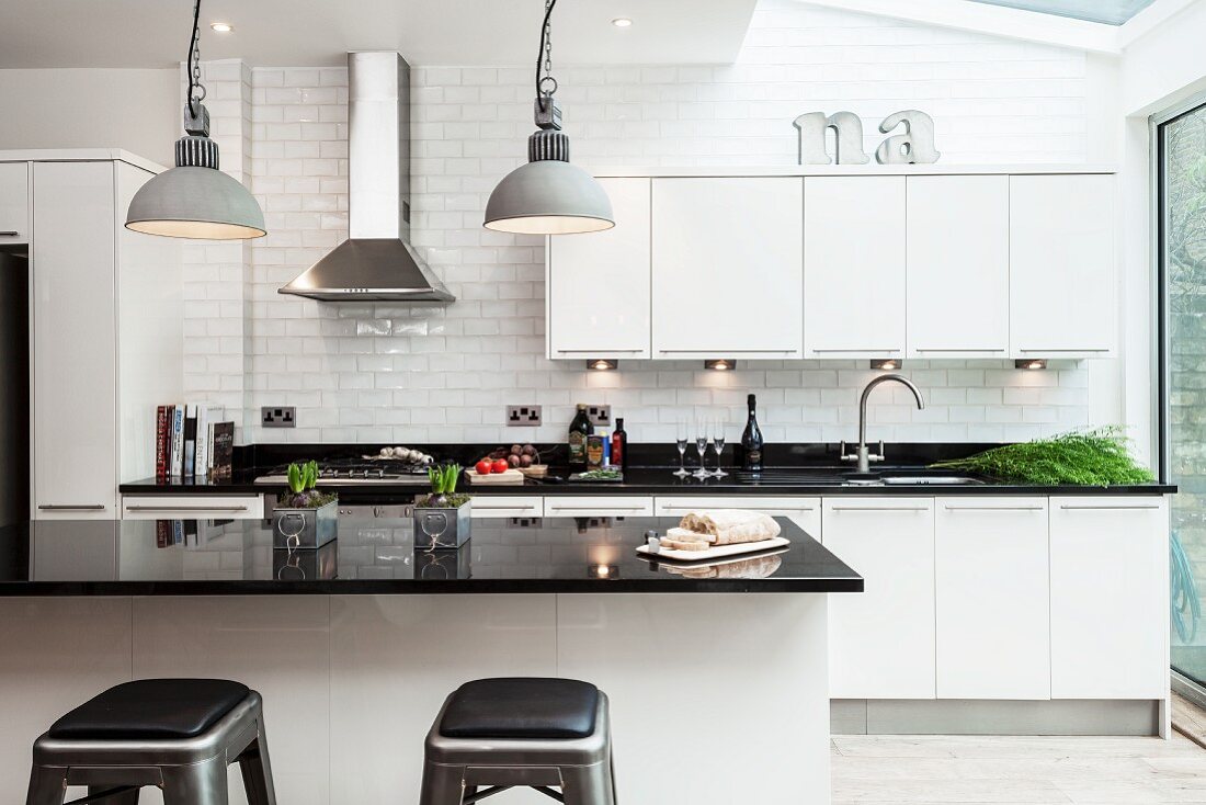 Mittelblock mit schwarzer, glänzender Arbeitsplatte in offener Designer Einbauküche mit weissen Schrankfronten