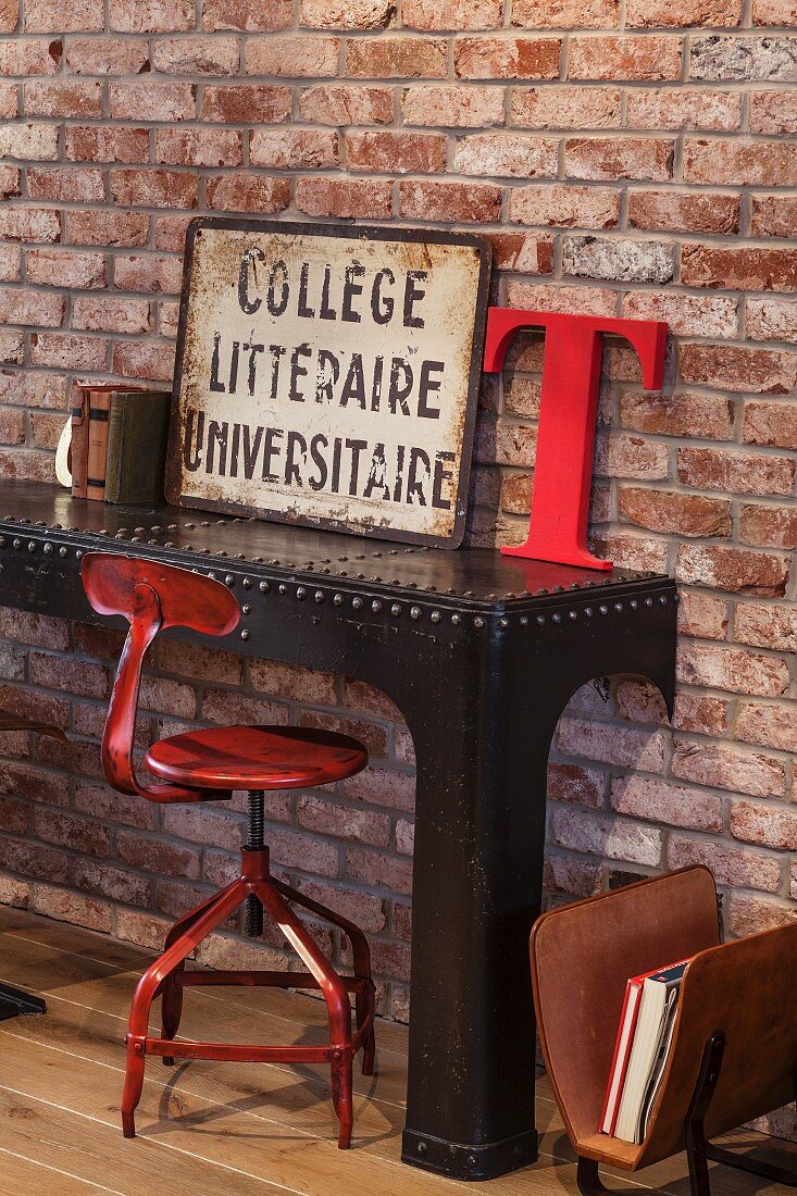 Rot lackierter Vintage Drehstuhl und schwarzer Metall Konsolentisch mit Deko-Objekten vor Ziegelwand