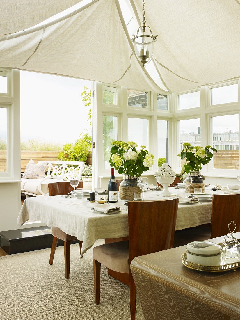 Set table below white awnings on ceiling in elegant conservatory with open terrace doors